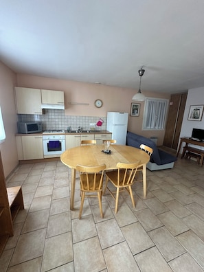 A compact kitchen with a dining table, chairs, a microwave, oven, and a refrigerator. - New Listing (Ramonchamp)