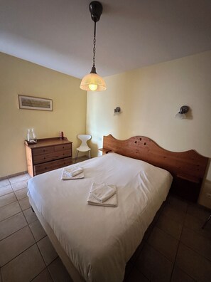 A hotel room with a bed, a wooden dresser, a chair, and a hanging light fixture.
