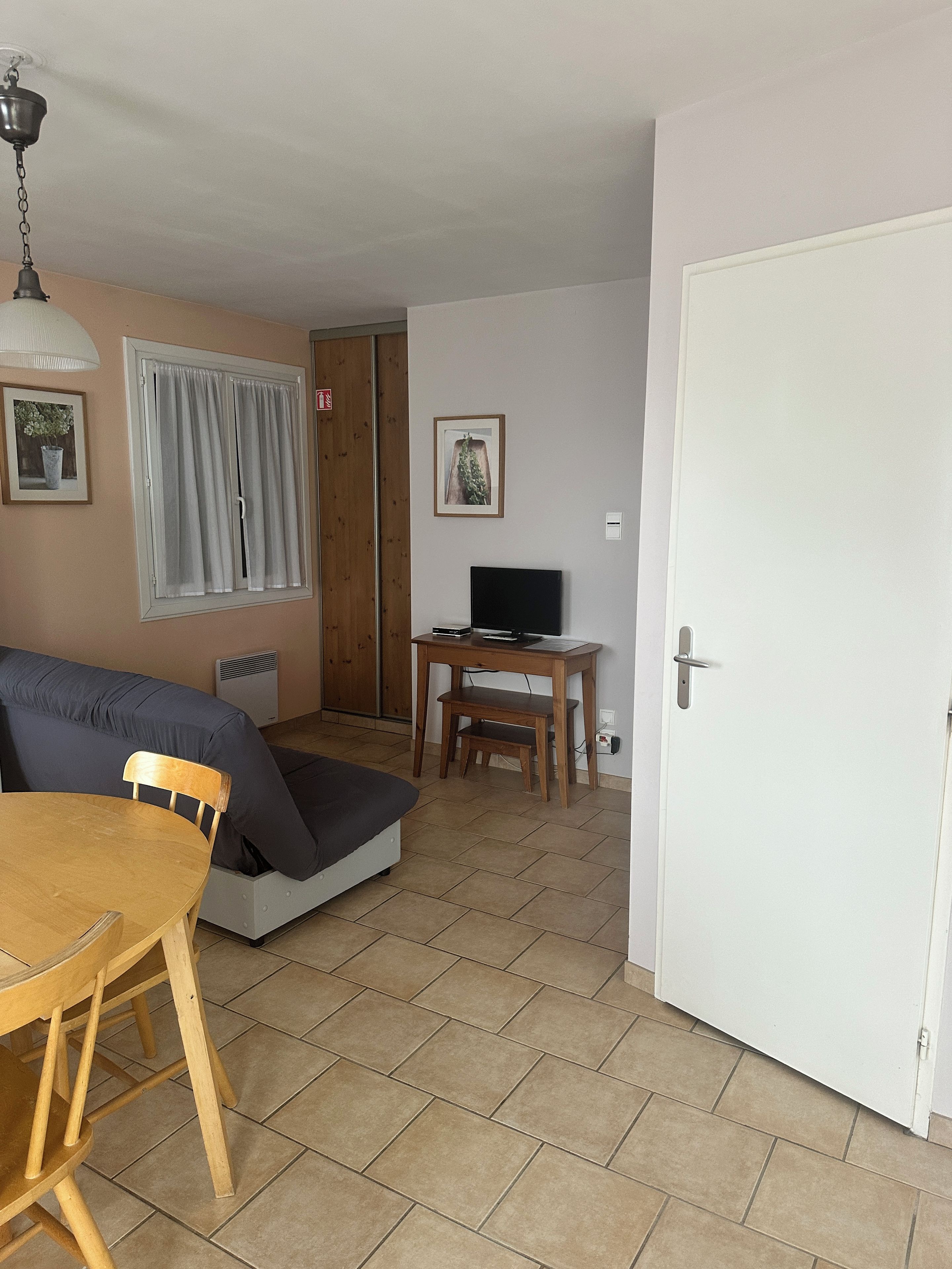 A living room with a sofa, a dining table, a TV on a wooden stand, and a door.