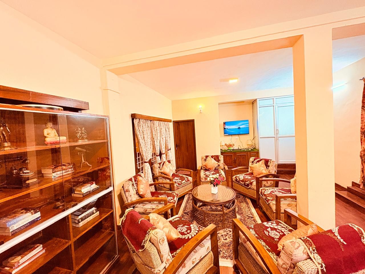 A well-lit living room with a television, comfortable seating, and a bookshelf.