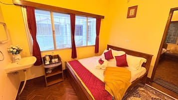 Habitación de hotel con cama, mesita de noche con lámpara, ventana con cortinas y un baño pequeño.