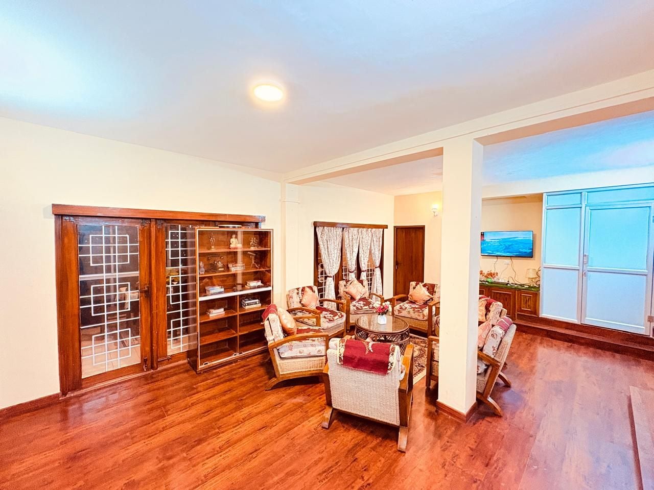 A spacious living room with a wooden floor, a dining area with a round table, and a built-in bookshelf.