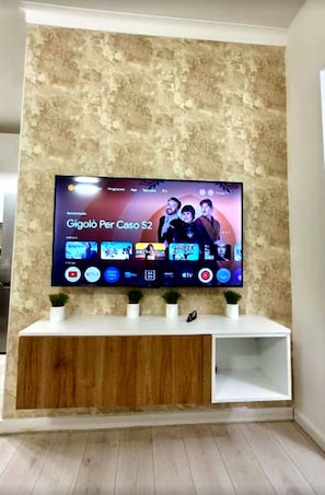 A flat-screen TV mounted on a textured wall with a wooden cabinet below. - New Listing (Milano)