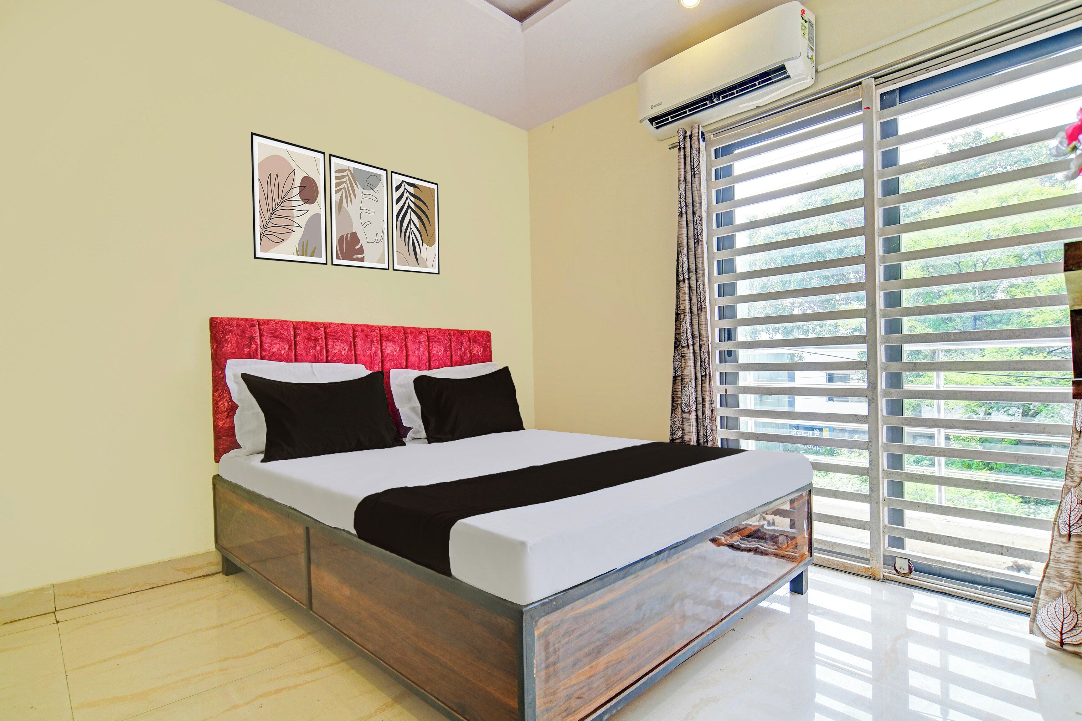 A bedroom with a bed, a headboard, a window with blinds, and wall-mounted air conditioning.