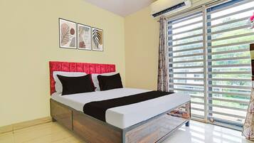 A bedroom with a bed, a headboard, a window with blinds, and wall-mounted air conditioning.