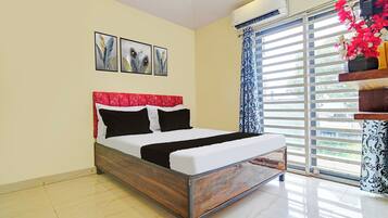 A bedroom with a bed, a window with blinds, and an air conditioning unit.