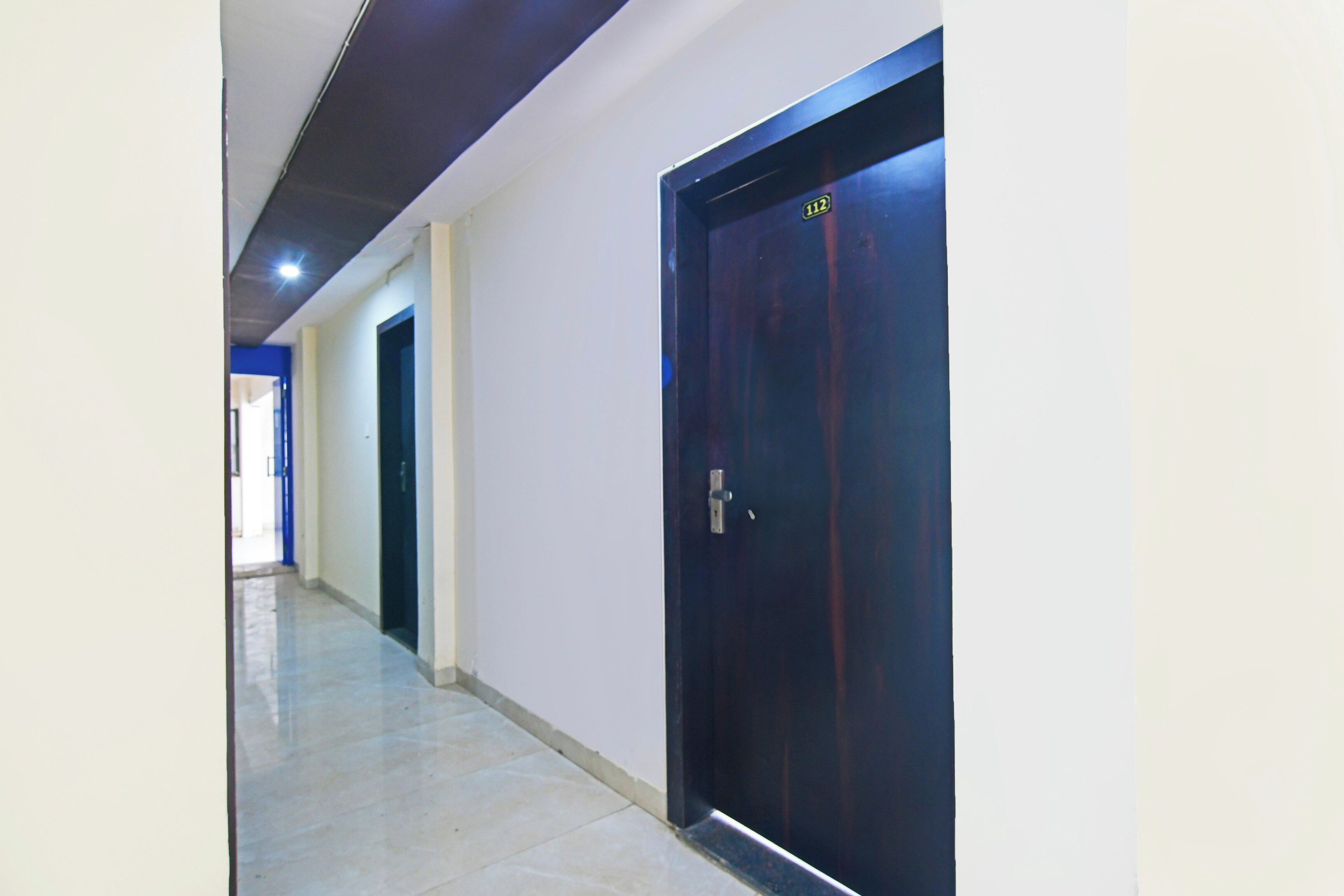 A corridor with a dark wooden door, white walls, and a tiled floor.