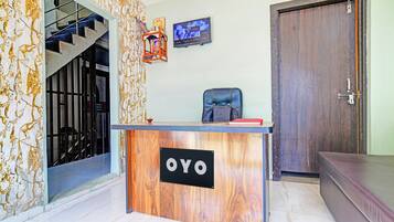 A reception desk with a sign reading 'OYO', a staircase, a door, and a wall-mounted television.