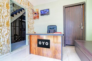 En receptionsdisk med skiltet 'OYO', en trappe, en dør og et tv ophængt på væggen.