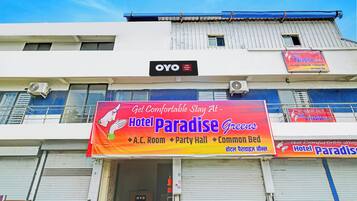 A hotel named 'Hotel Paradise Greens' with a signboard advertising A.C. Room, Party Hall, and Common Bed.