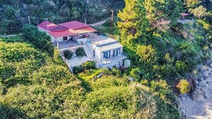 A two-story house with a red roof, surrounded by dense greenery and a hillside. - Holiday Home 'Art Of Luxury' with Sea View, Private Terrace and Air Conditioning (Κάτω Πολυδένδρι)
