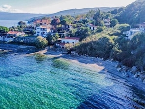 Eine Küstenstadt mit Gebäuden entlang der Uferlinie, blauem Wasser und Hügeln im Hintergrund.