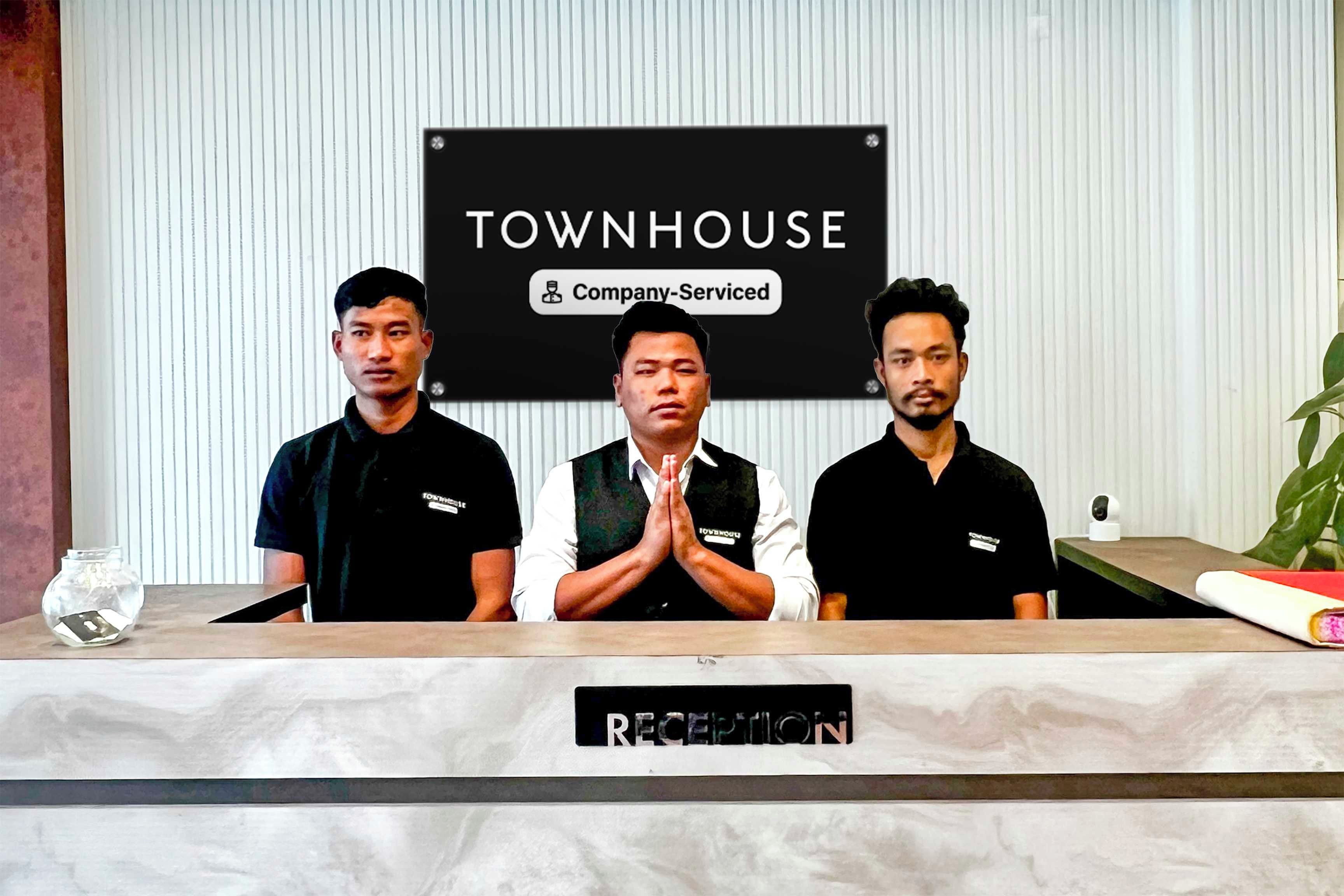 Tres personas de pie detrás de un mostrador de recepción con un cartel que dice 'TOWNHOUSE Company-Serviced'.
