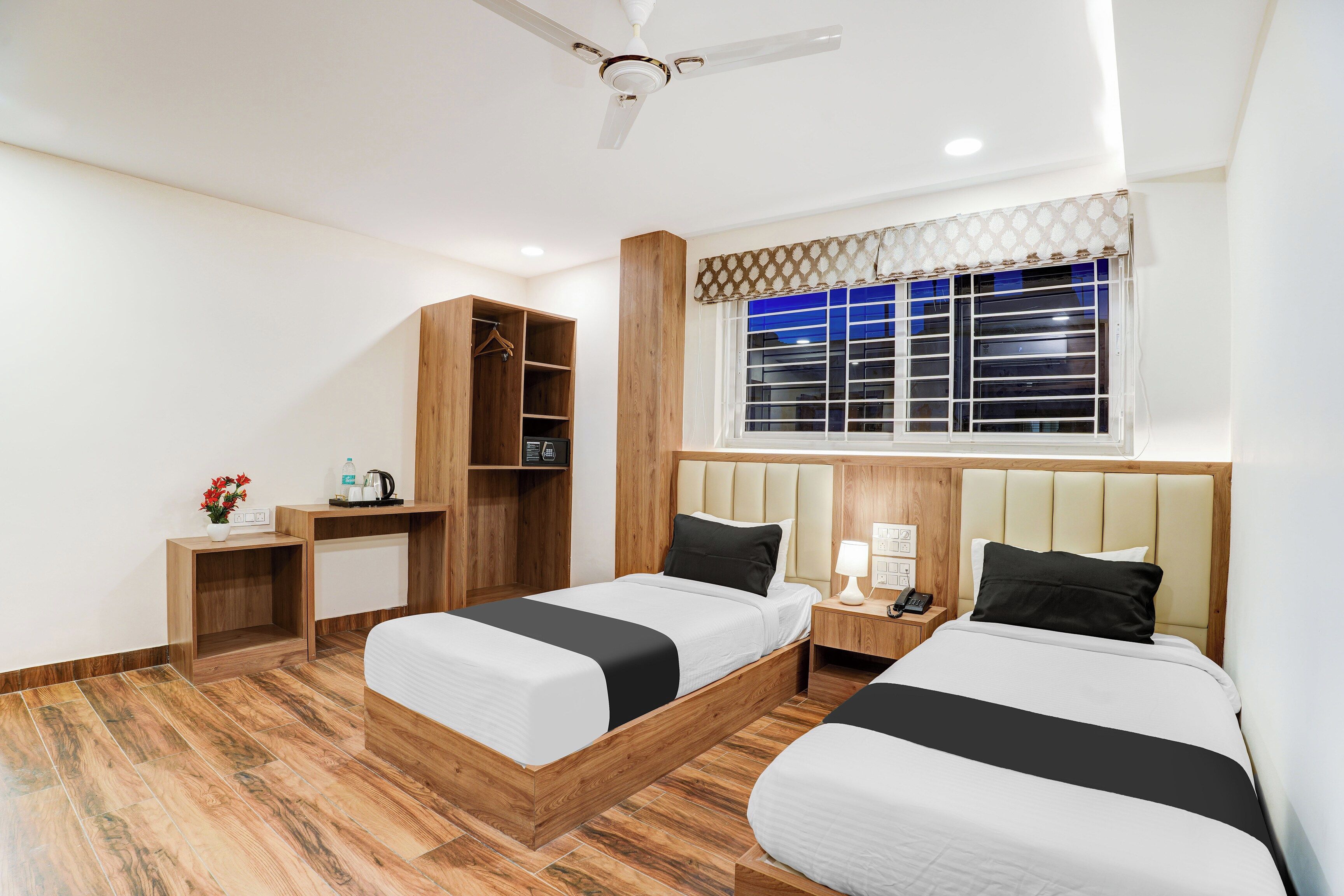 Habitación de hotel con dos camas, un armario de madera, un escritorio, una ventana con persianas y un ventilador de techo.
