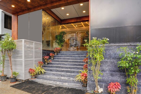 Una escalera conduce a la entrada de un edificio, con plantas en macetas y una reja de metal.