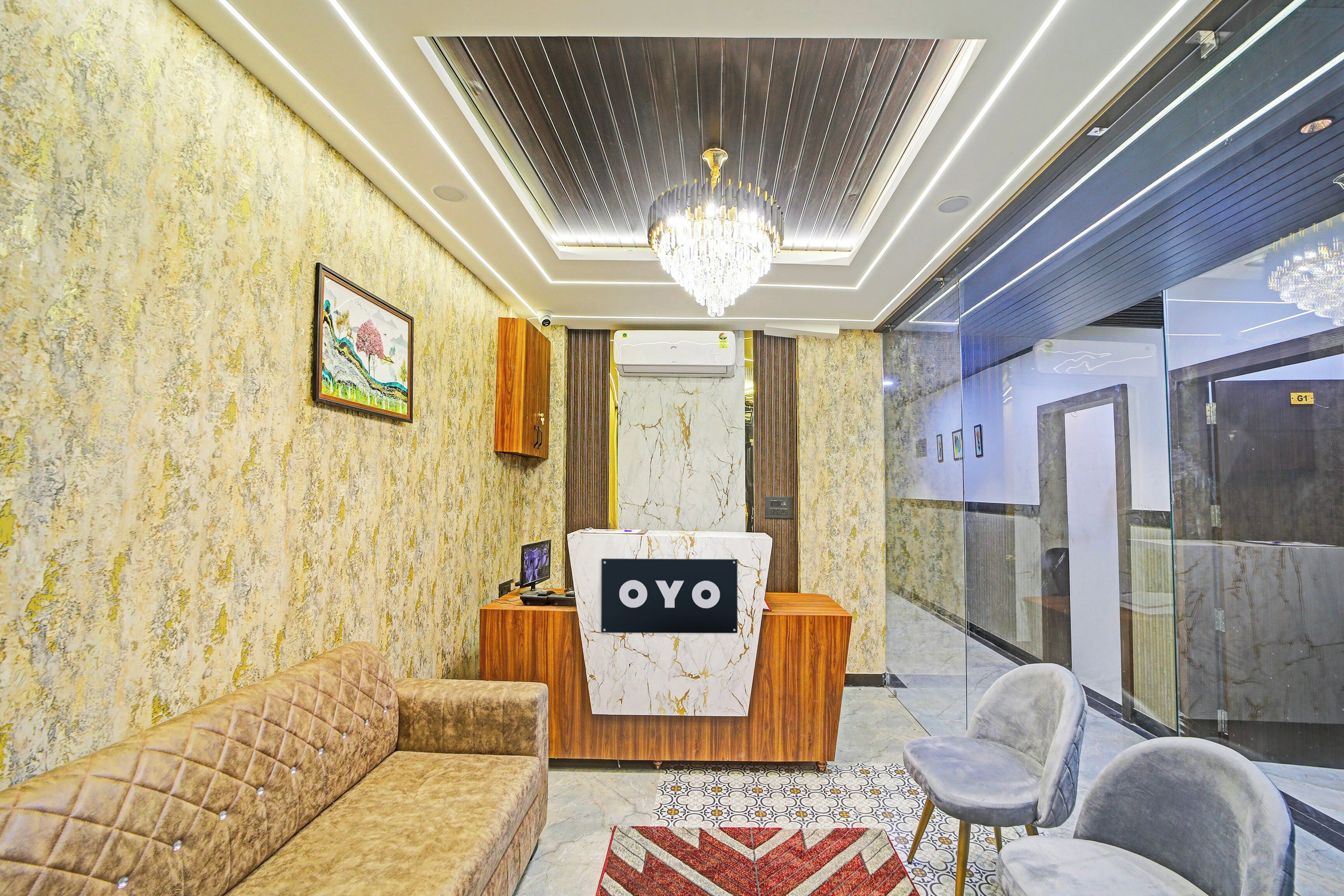 A reception area with a wooden reception desk labeled 'OYO', a plush sofa, a chandelier, and a patterned wall.