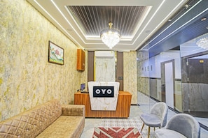 Et receptionsområde med en træreception disk markeret 'OYO', en blød sofa, en lysekrone og en væg med et mønster.