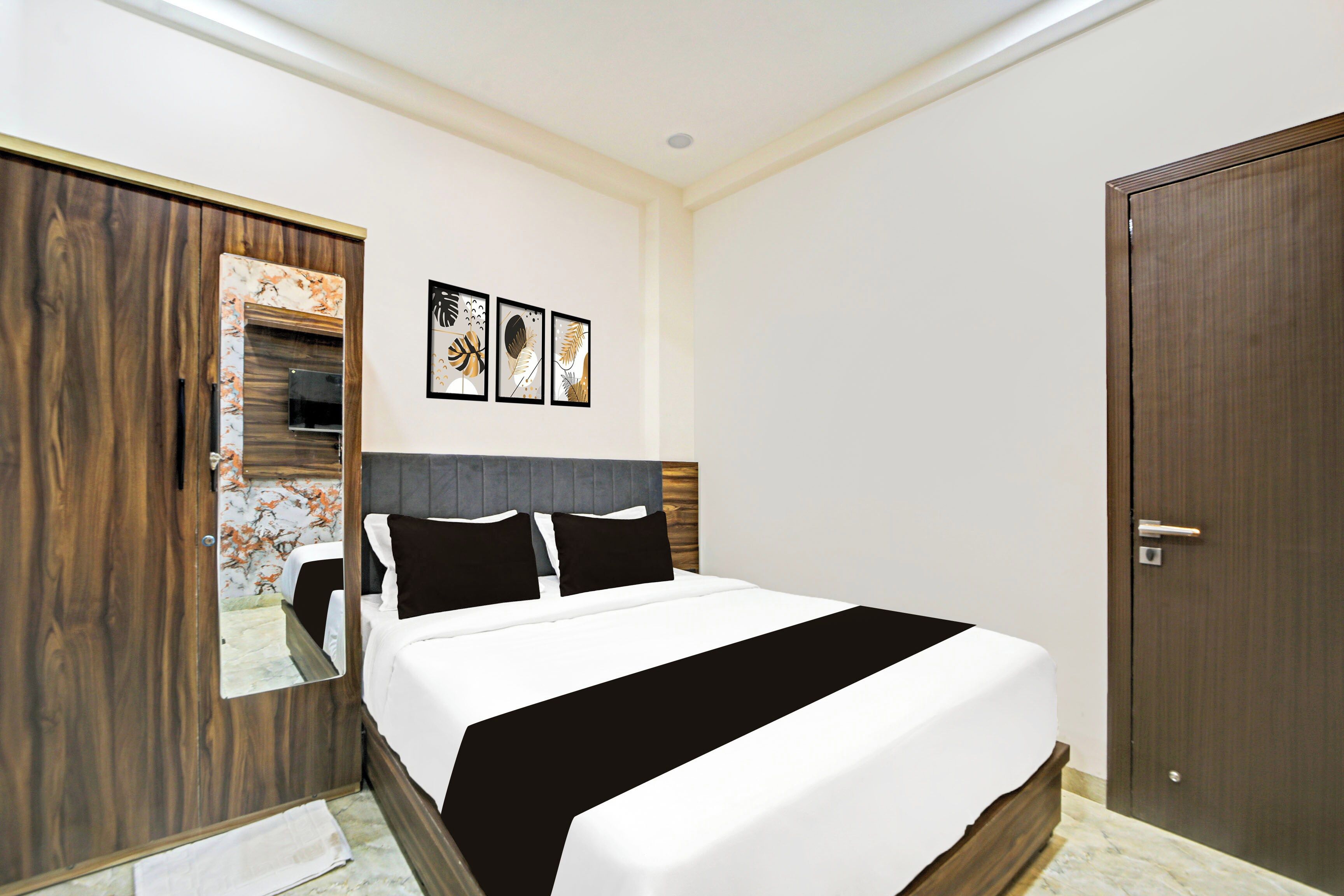 A bedroom with a bed, a wardrobe, a mirror, and three framed pictures on the wall.