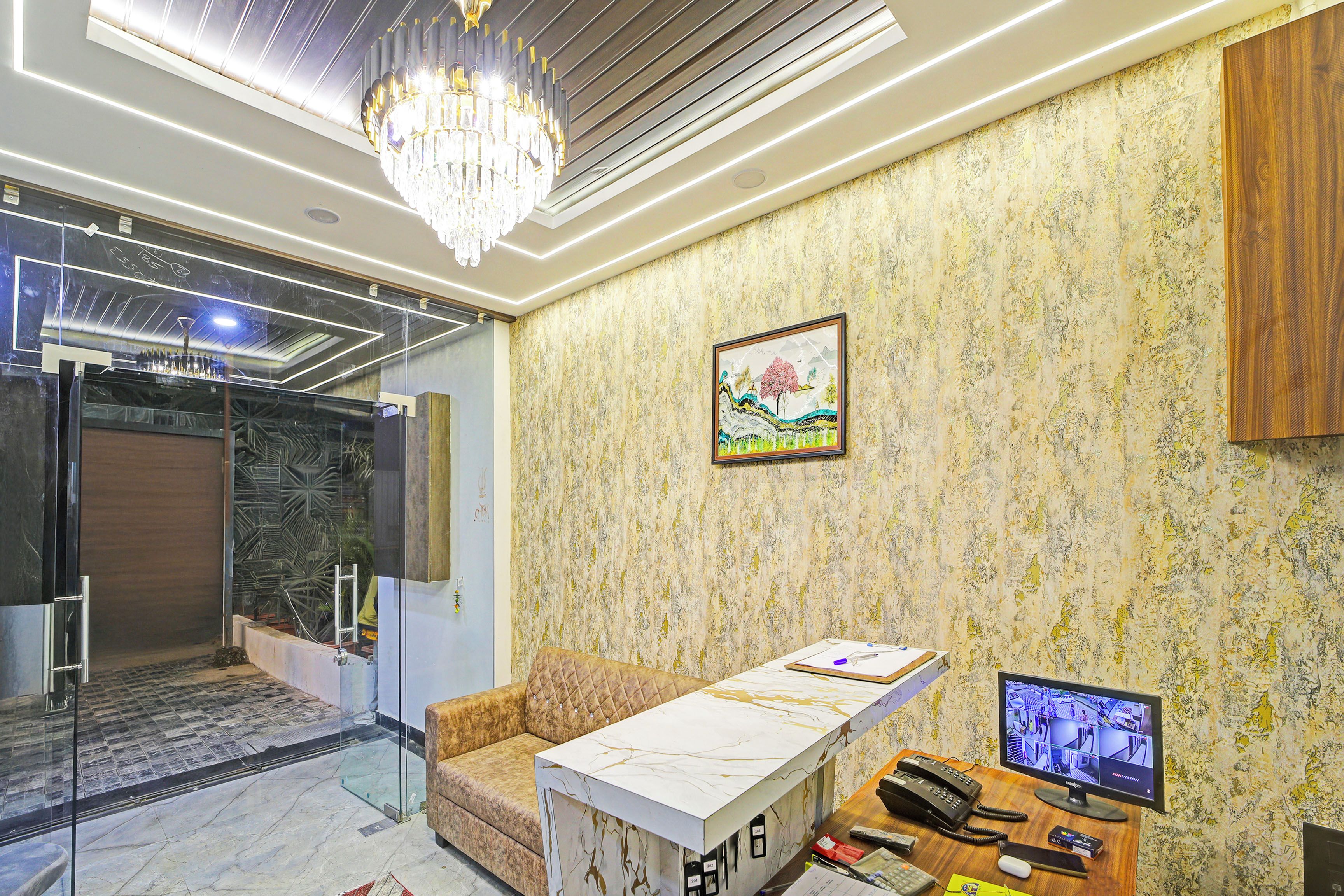 Un interior moderno con pared de diseño marmolizado, una obra de arte enmarcada, un área de estar acolchada y un escritorio con monitor de computadora.