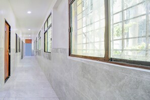 A long, narrow hallway with large windows on one side, allowing natural light to enter. - Hotel O katyayani (Indore)