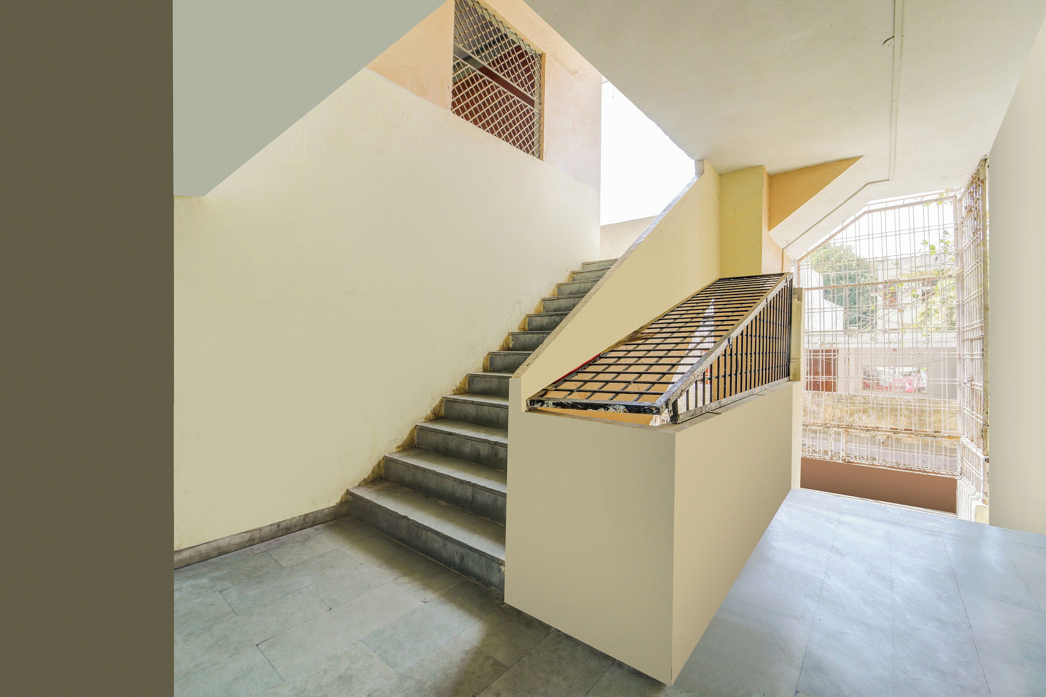 Una escalera con barandilla de metal y vista al exterior a través de una ventana con barrotes.