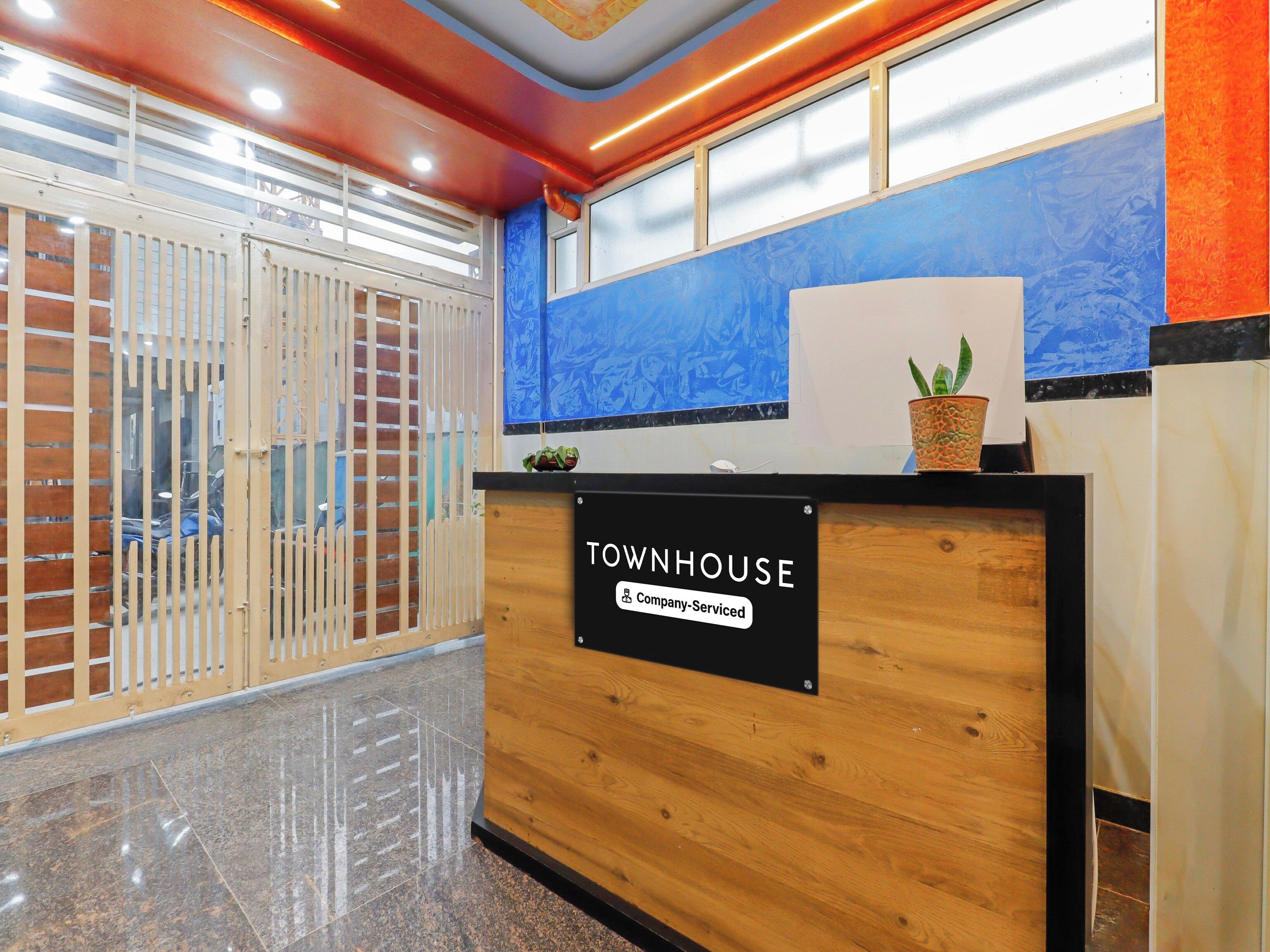 Una recepción con el cartel 'TOWNHOUSE', señalización de la empresa, una planta en maceta y vistas a una pared azul con una ventana.