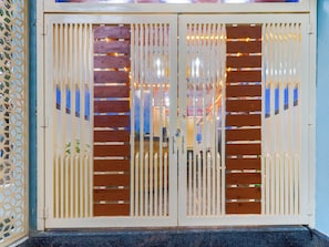 Puertas dobles con listones verticales y una mirilla, que dan acceso a un espacio interior con una pared azul y un suelo estampado.