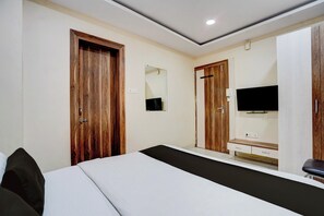 Habitación de hotel con una cama, televisor, cómoda y puertas de madera.