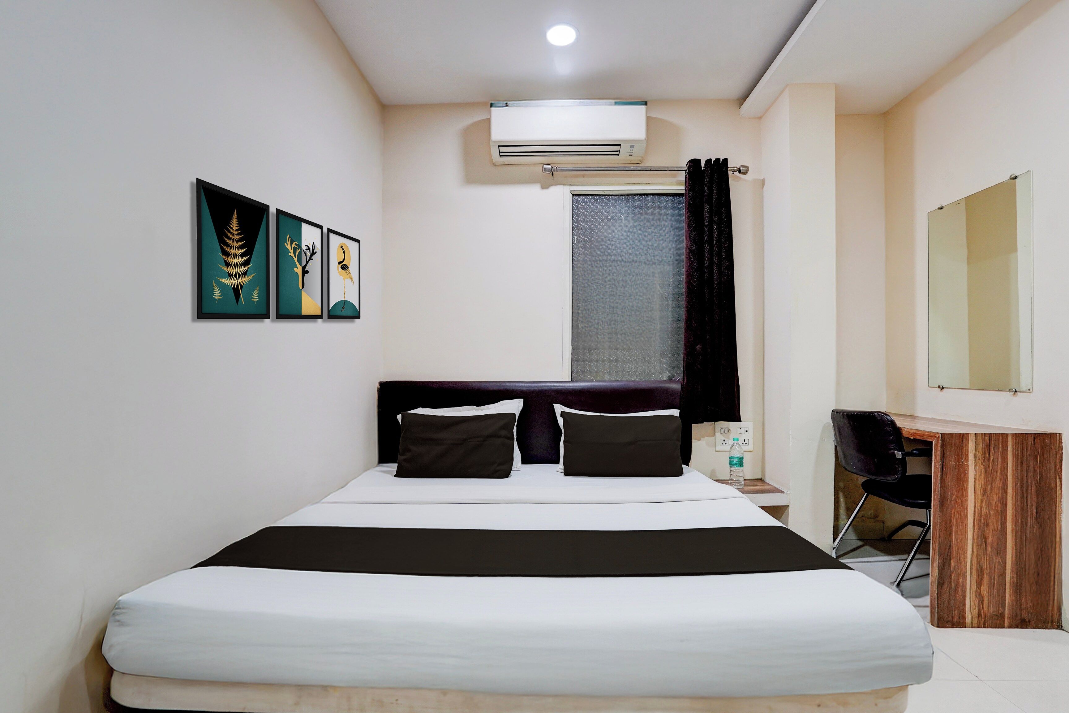 A hotel room with a bed, a desk, a chair, an air conditioning unit, and artwork on the wall.