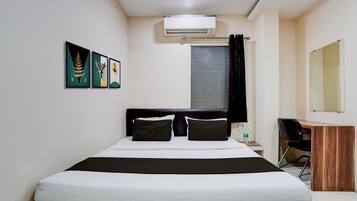A hotel room with a bed, a desk, a chair, an air conditioning unit, and artwork on the wall.