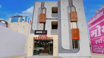 Um hotel moderno com uma placa grande de 'OYO Hotel S.P. Residency', uma entrada espaçosa e uma fachada marcante com ripas verticais de madeira.