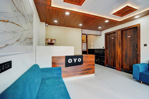 A reception area with a wooden reception desk labeled 'OYO,' a marble wall, a blue sofa, and a large wooden door.