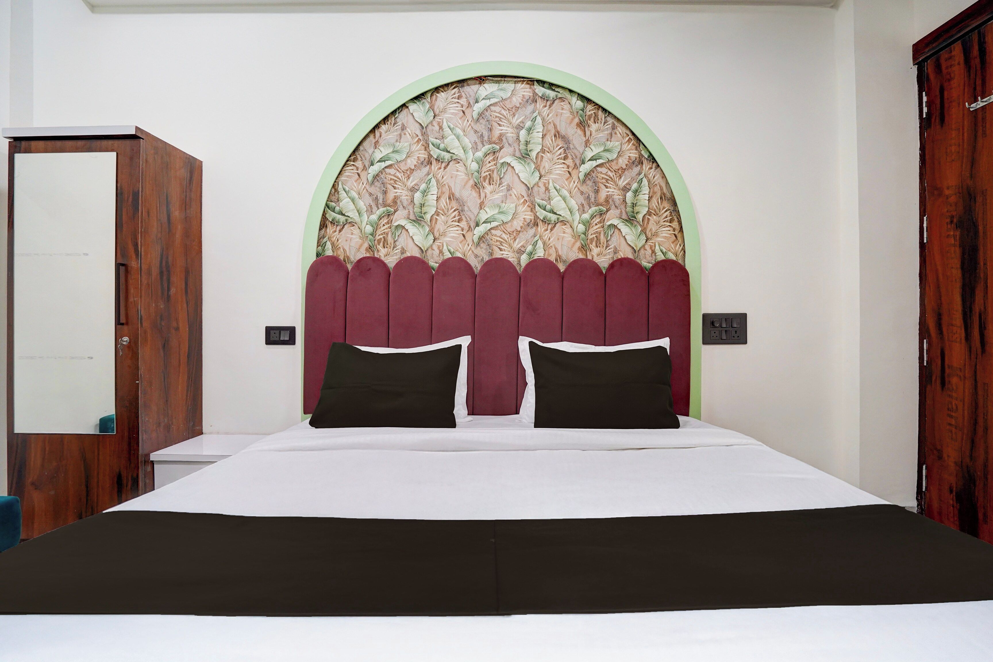Quarto com uma cama, porta de madeira e parede com desenho de folhas.