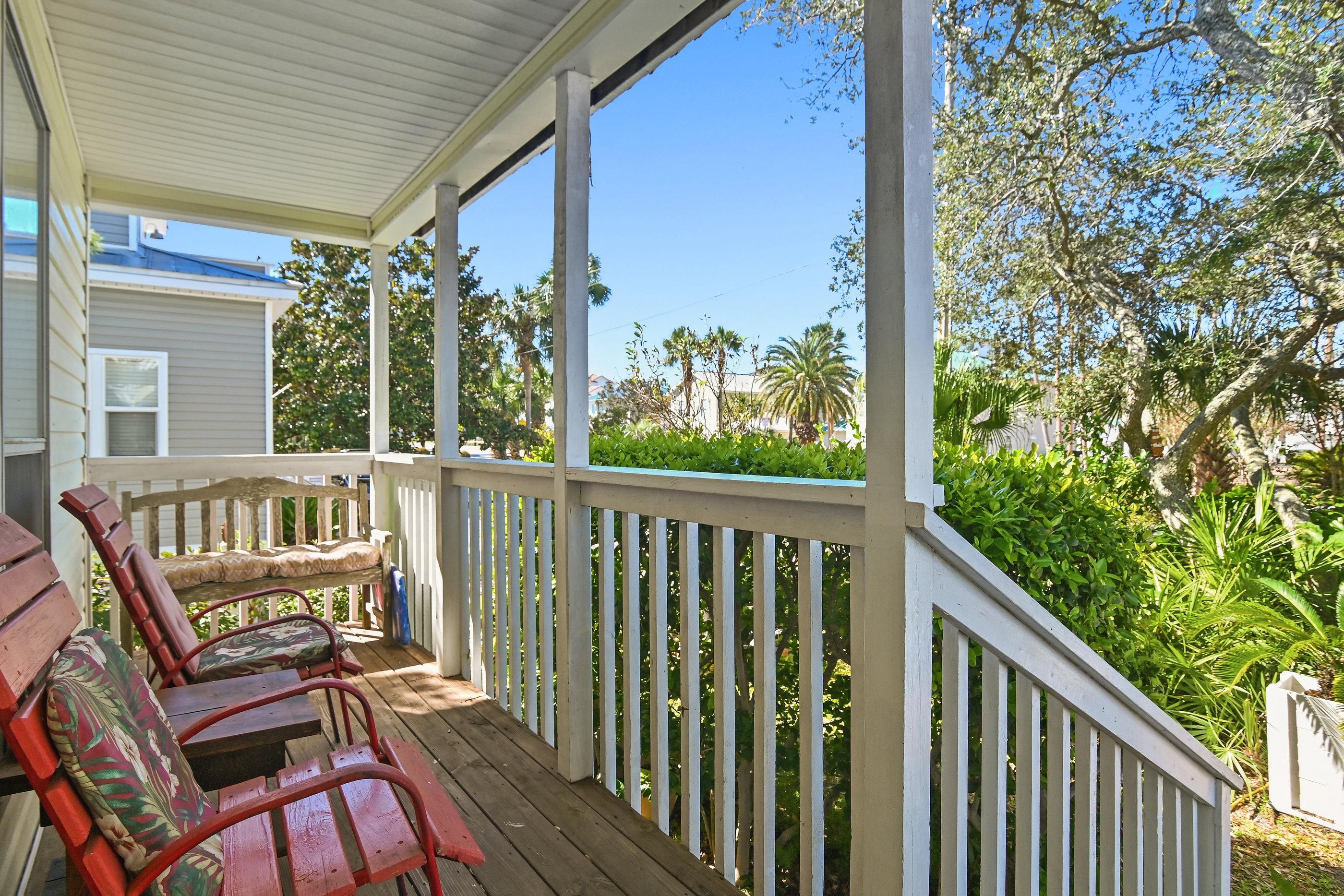 A covered porch with wooden railings, a bench, and two chairs.