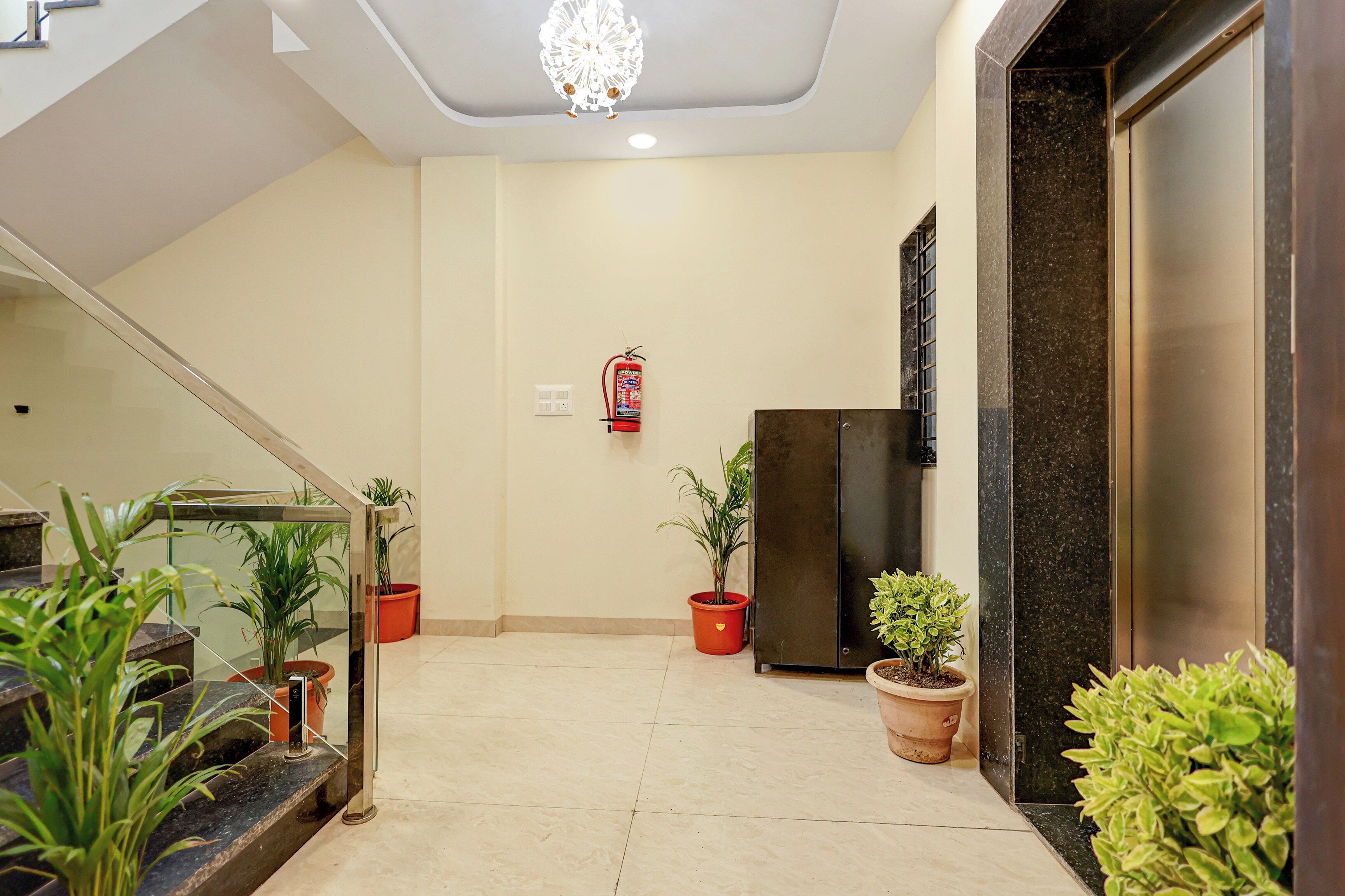 Hall de hotel com escada, extintor de incêndio e plantas em vasos.