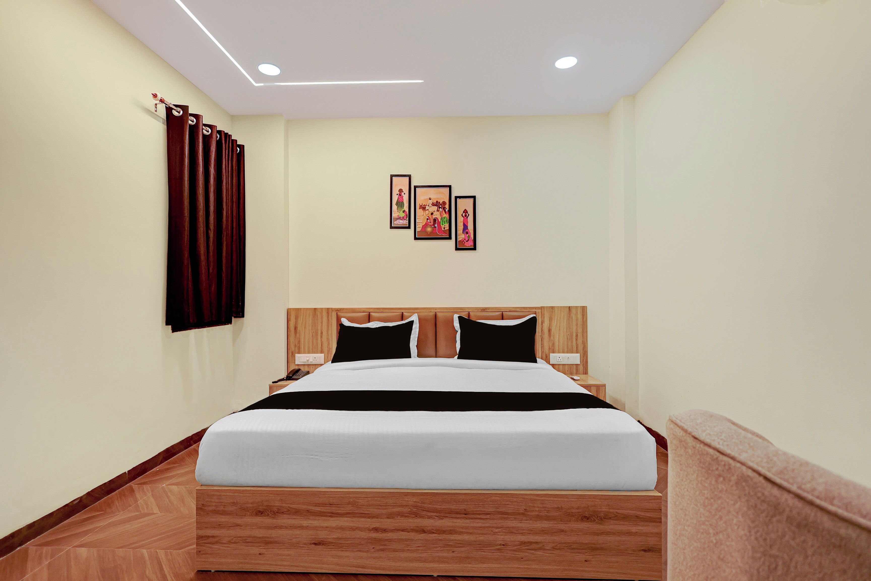 A hotel room with a wooden bed, a headboard, a bedside table, a telephone, and a wall with three framed pictures.