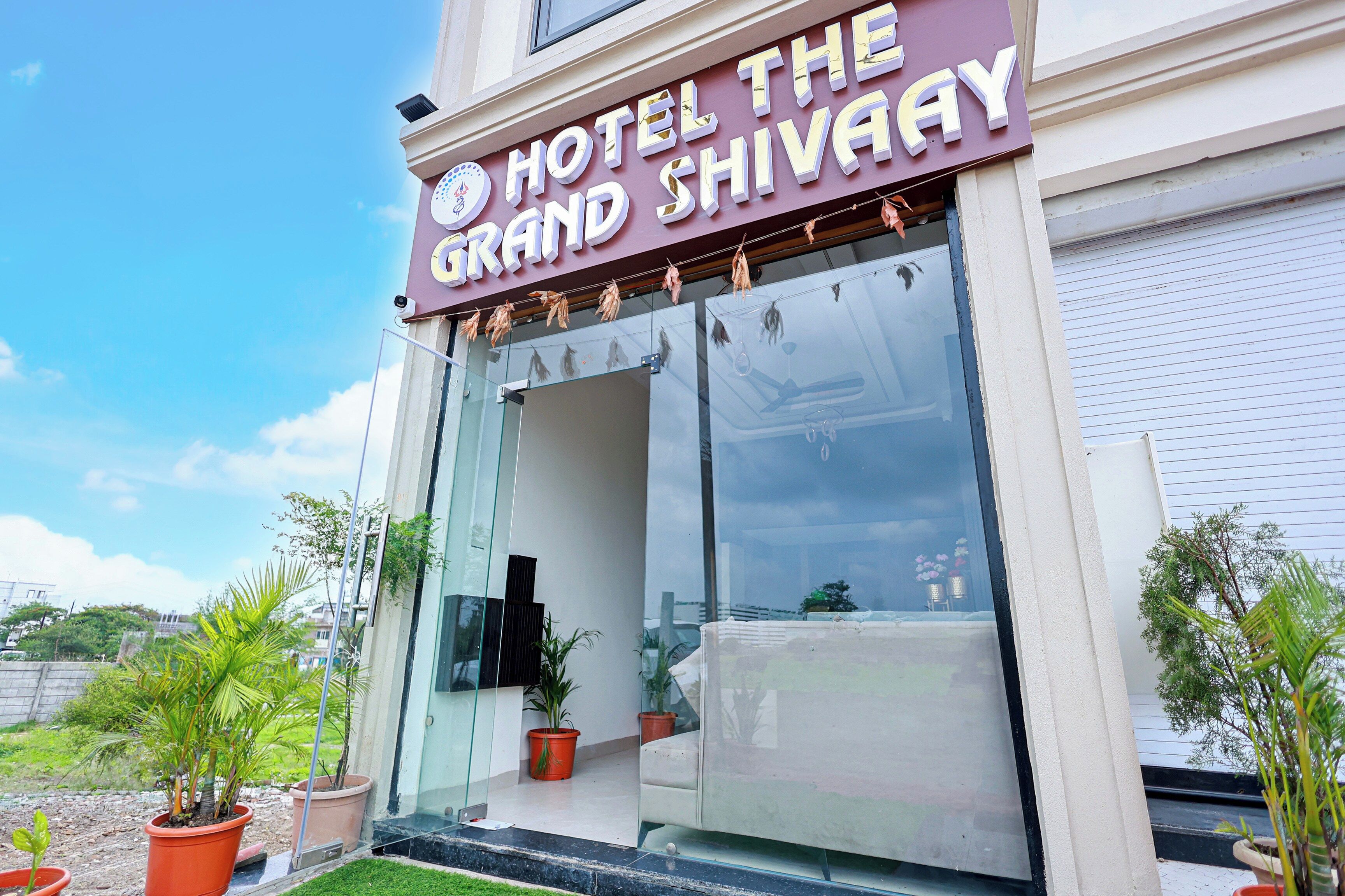 The exterior of Hotel The Grand Shivay with a clear entrance and potted plants outside.