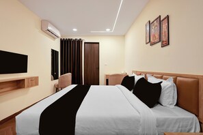 Habitación de hotel con cama, televisor de pantalla plana, aparador de madera, escritorio, silla, puerta y pared con cuadros enmarcados.