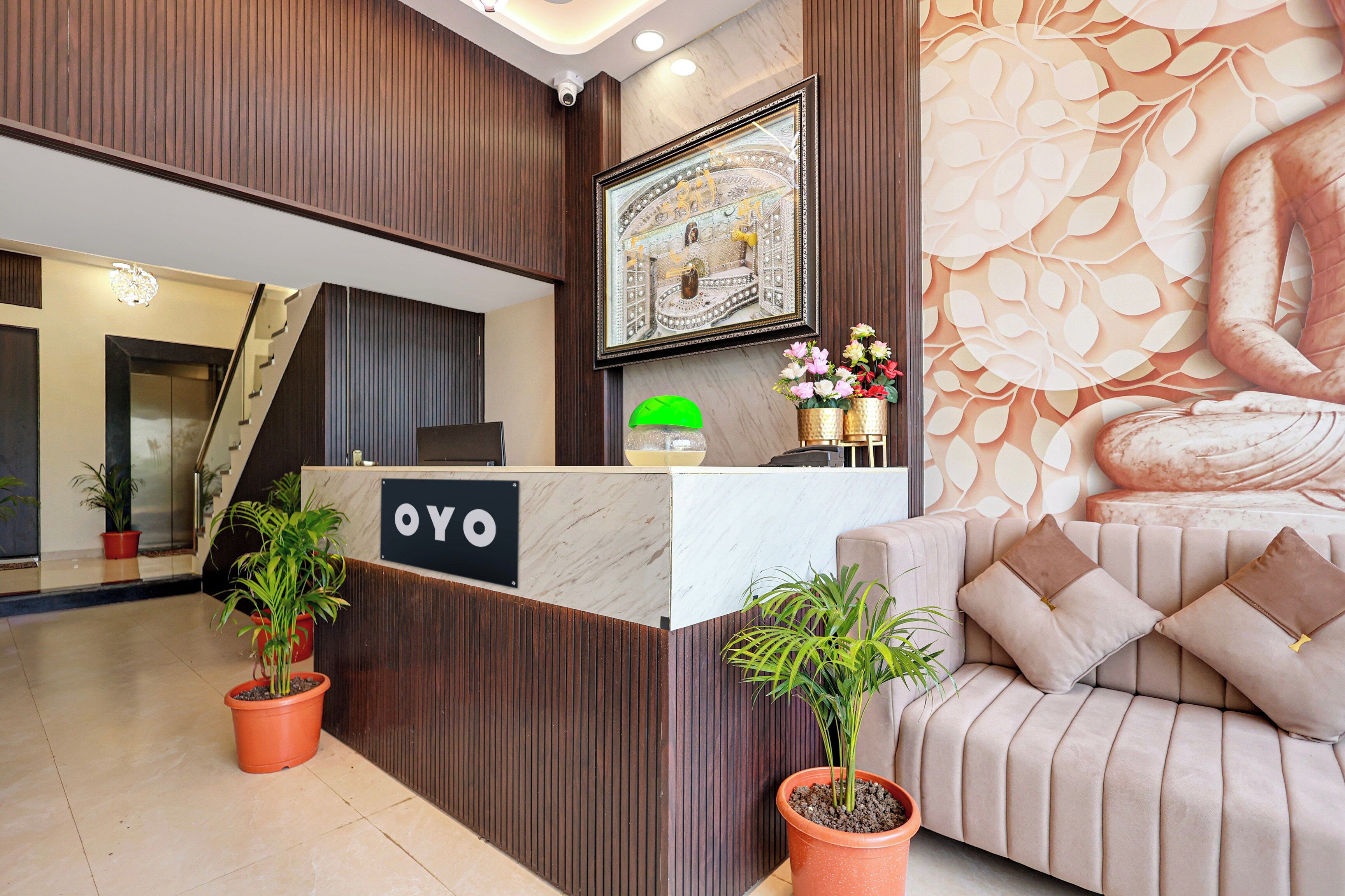 Bancada de recepção com a placa 'OYO', ladeada por plantas em vasos, um sofá com almofadas e uma parede decorativa com padrão de folhas.