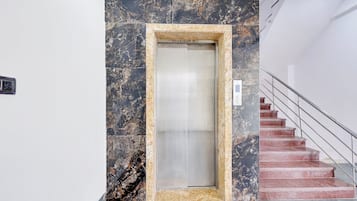 Un ascensor con pared de mármol y escalera con barandillas de metal.