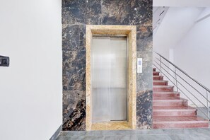 Un ascensor con pared de mármol y escalera con barandillas de metal.