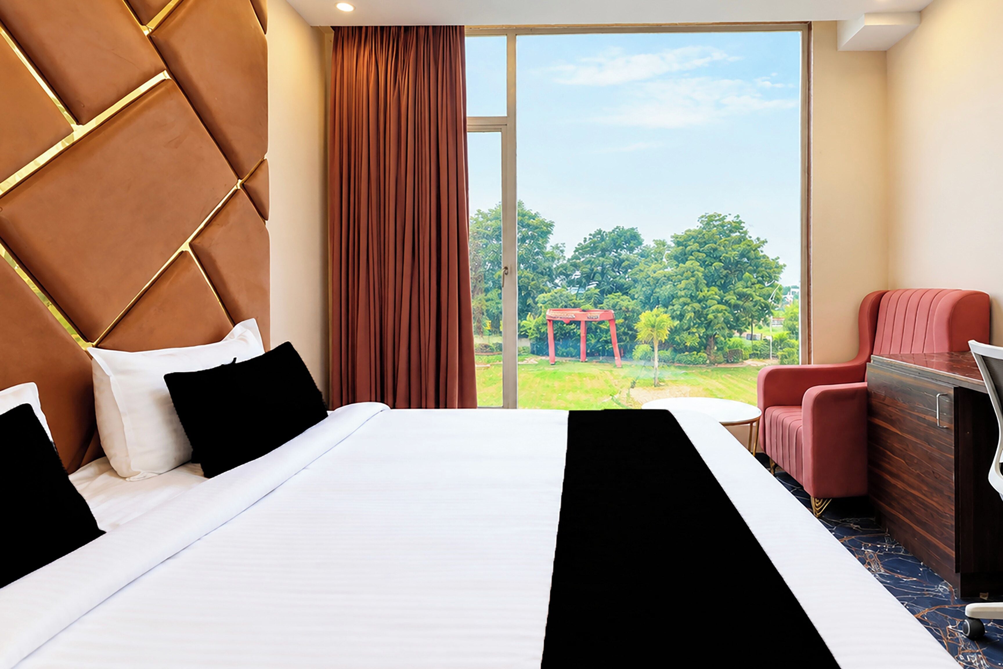 Habitación de hotel con una cama grande, un sillón rojo, un aparador de madera y vistas a un jardín.