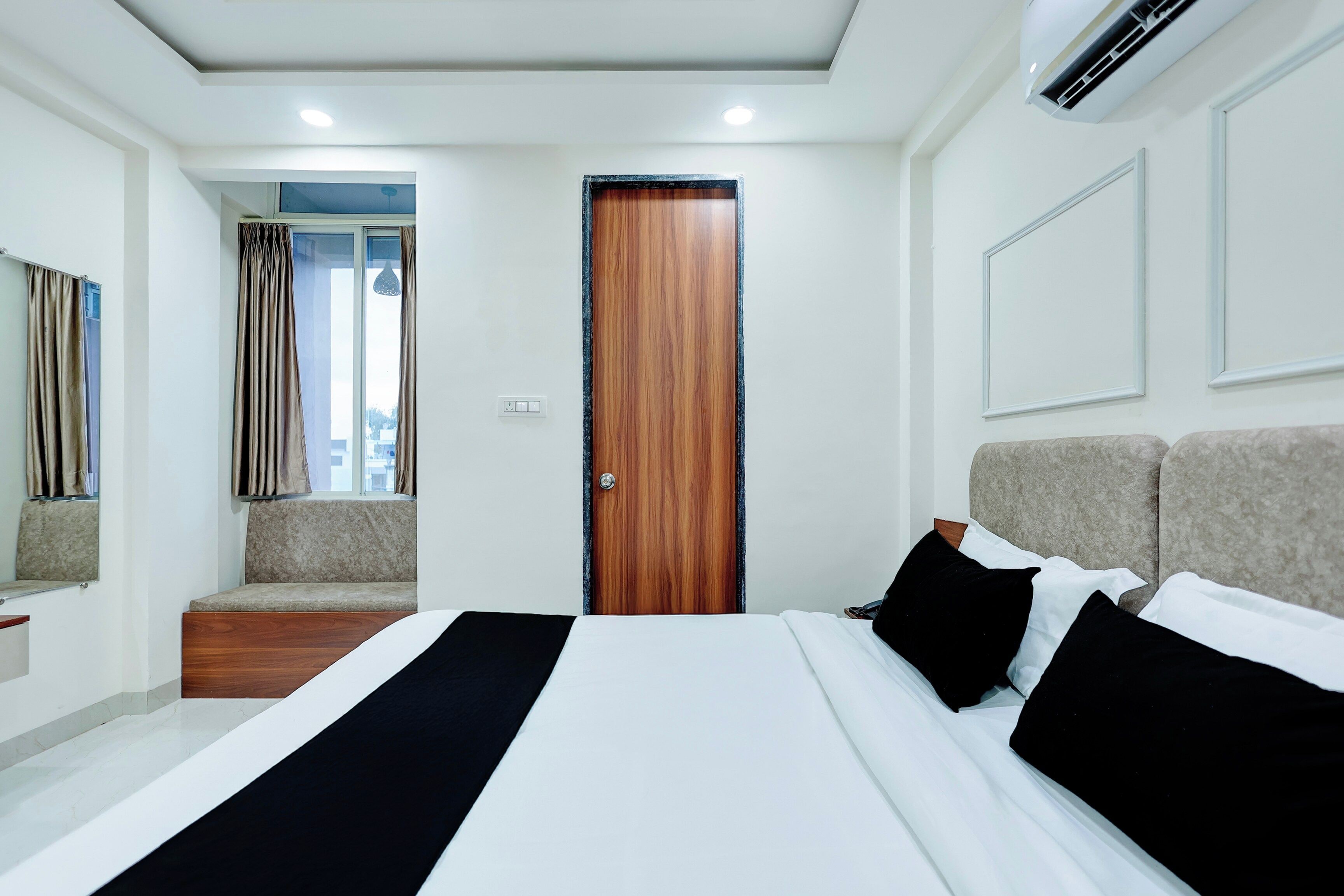 Una habitación de hotel con una cama, un banco, una puerta y un equipo de aire acondicionado.