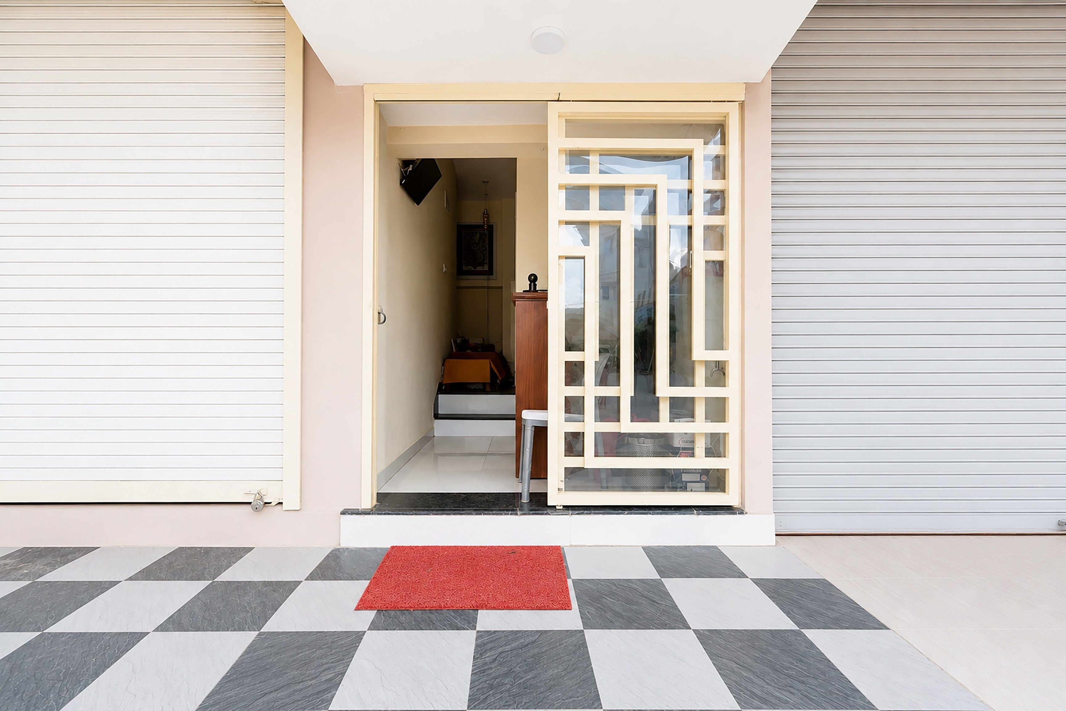 Una entrada residencial con una puerta de garaje cerrada, un felpudo rojo y un piso con diseño de cuadros.
