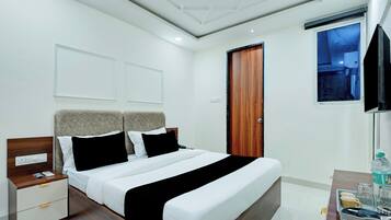 A hotel room with a bed, bedside tables, a nightstand, a wooden door, a window, and a television.