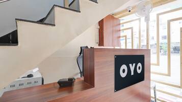 A reception desk with a sign that reads 'OYO' in a modern hotel lobby with a staircase and large windows.
