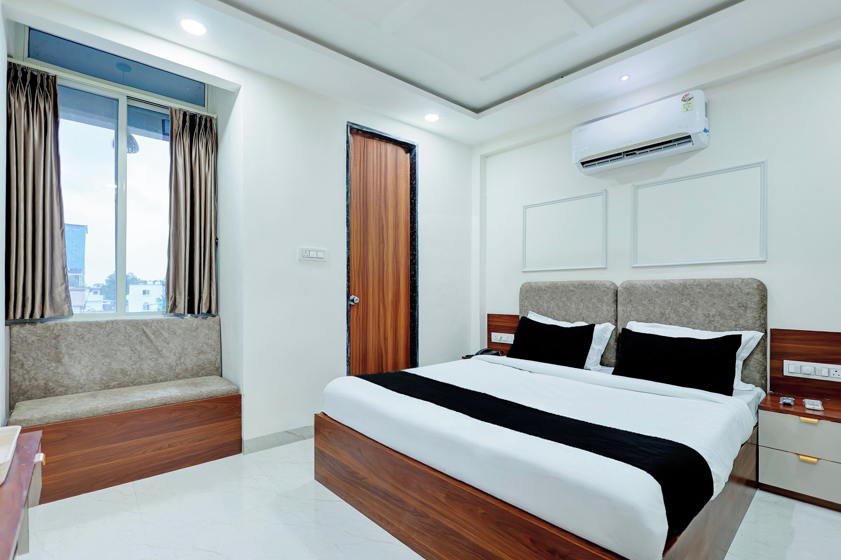 Habitación de hotel con cama, ventana con cortinas, equipo de aire acondicionado y vista a edificios.