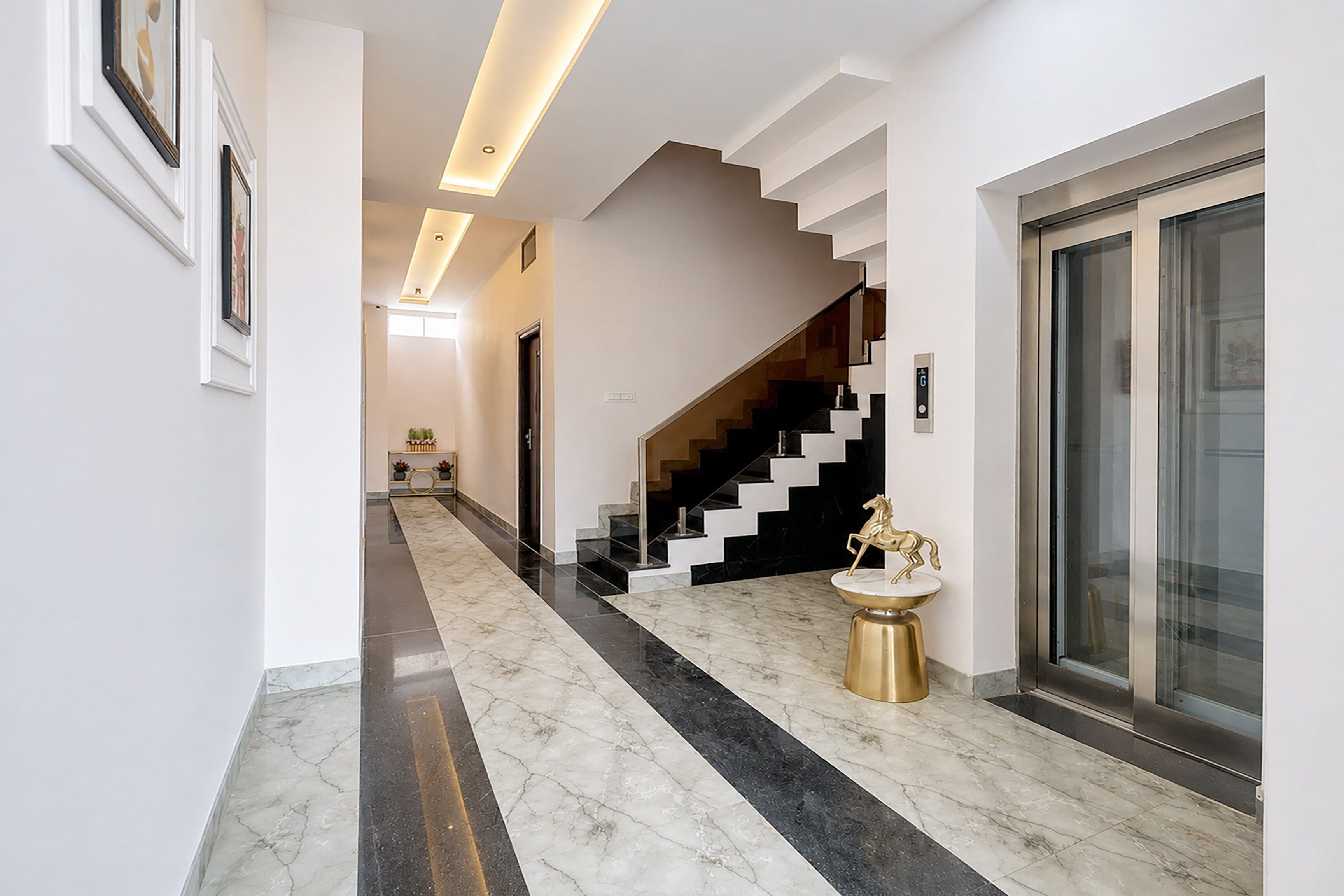 Un interior moderno con suelo de mármol, una escalera y la puerta de un ascensor de vidrio.