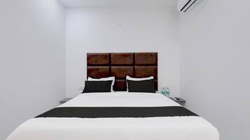 Una habitación de hotel con una cama, una mesita de noche, un equipo de aire acondicionado y una botella de agua.
