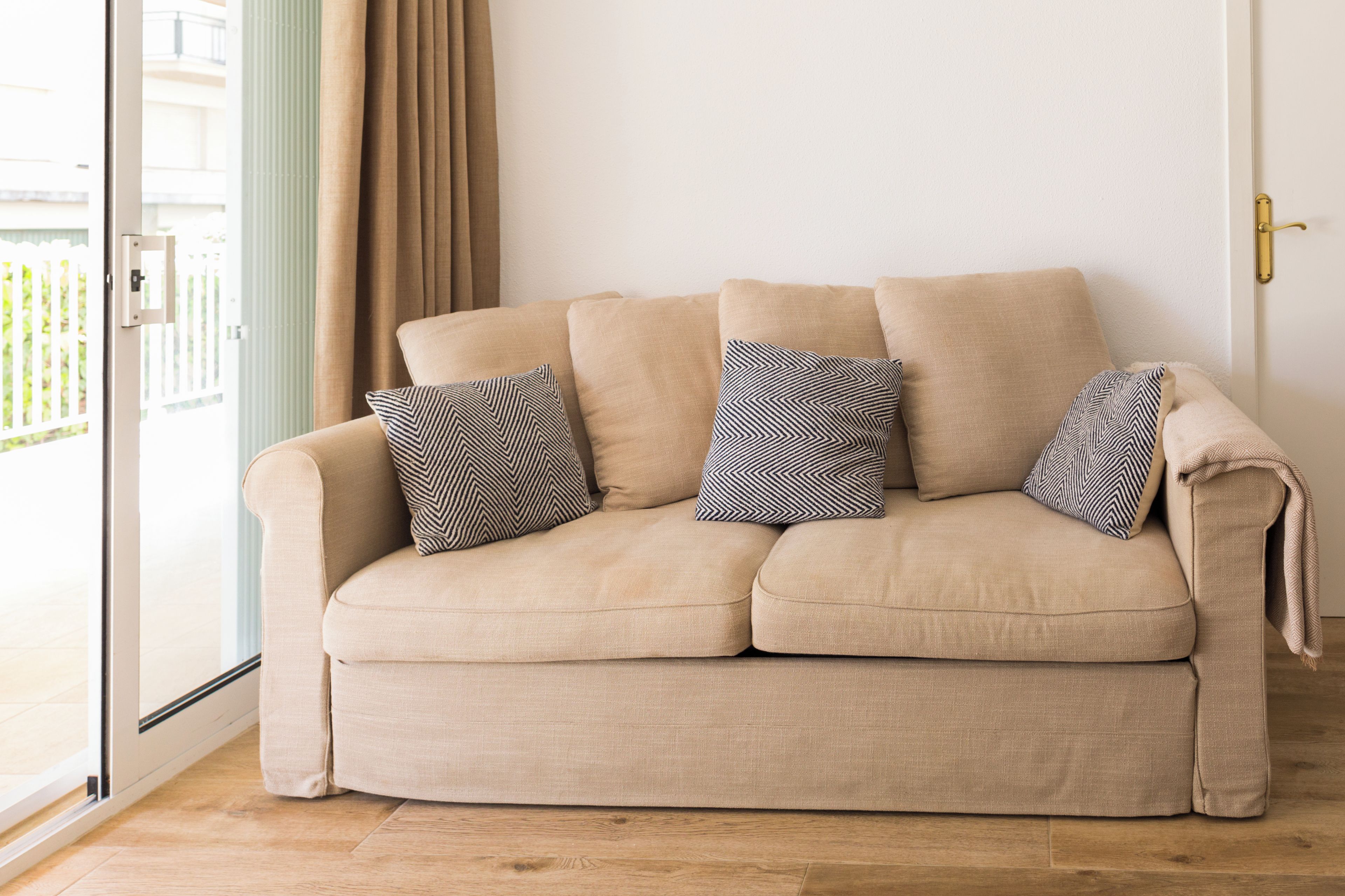 Un canapé beige agrémenté de coussins à motifs, une porte en verre et un plancher en bois.